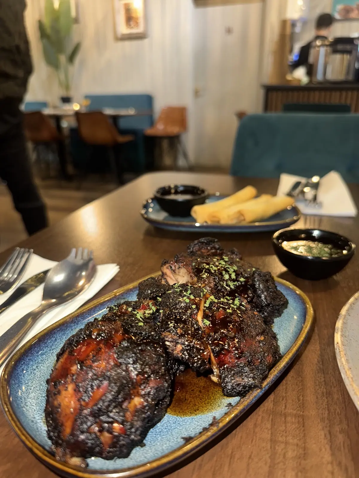 The teal-and-timber dining room with a platter of jerk chicken on the laid table in the foreground